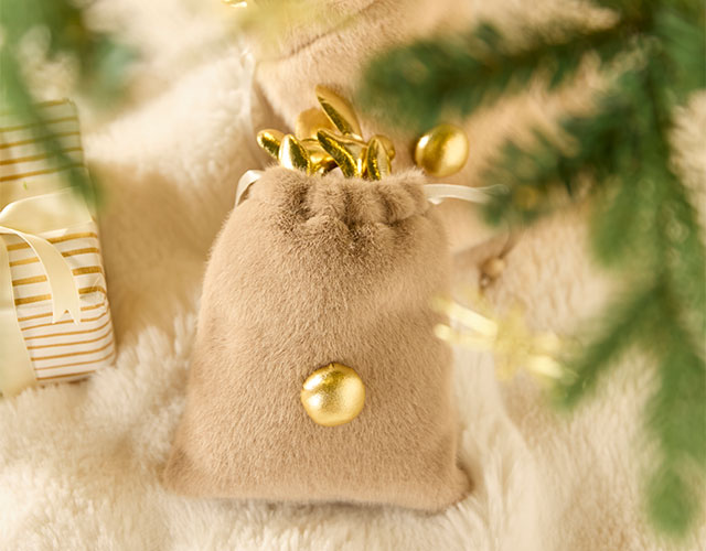 Décoration de Noël : petit sac en velours beige avec des boules de Noël dorées posées sur une fourrure douce