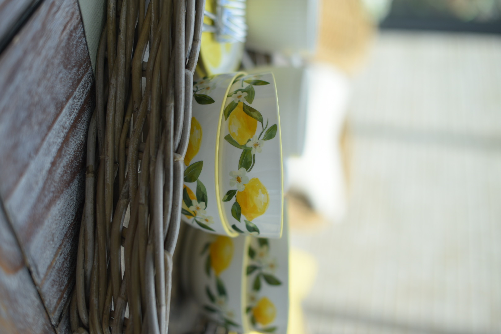 Vaisselle : bol en céramique blanche orné d'un motif de citrons, présenté dans un panier en rotin tressé, pour une décoration de table estivale
