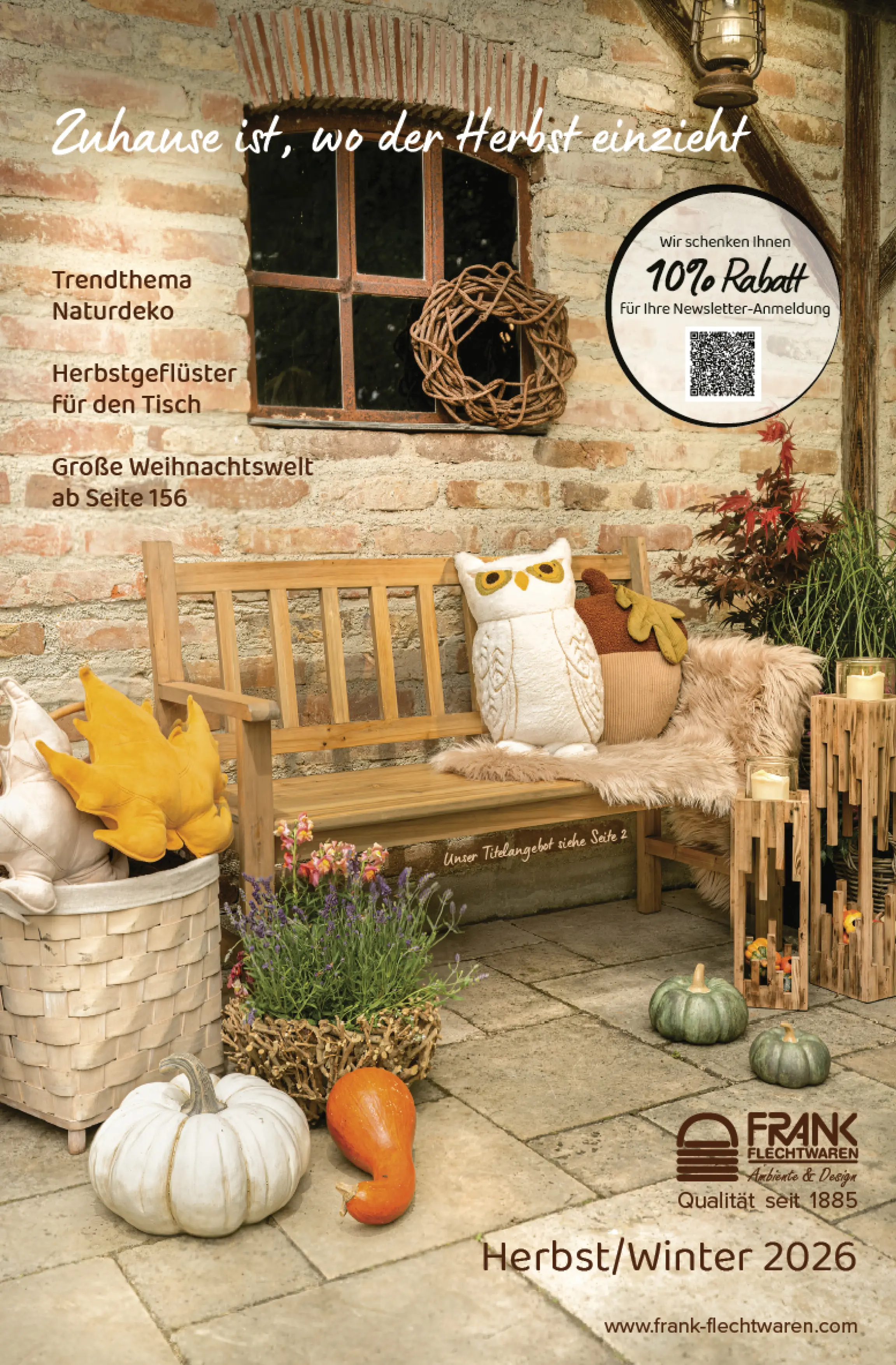 Décoration d'automne pour terrasse avec banc en bois, citrouilles, coussins en forme de chouettes, lanternes, panier tressé et matériaux naturels devant un mur rustique en briques, illustration de couverture du catalogue automne/hiver 2026