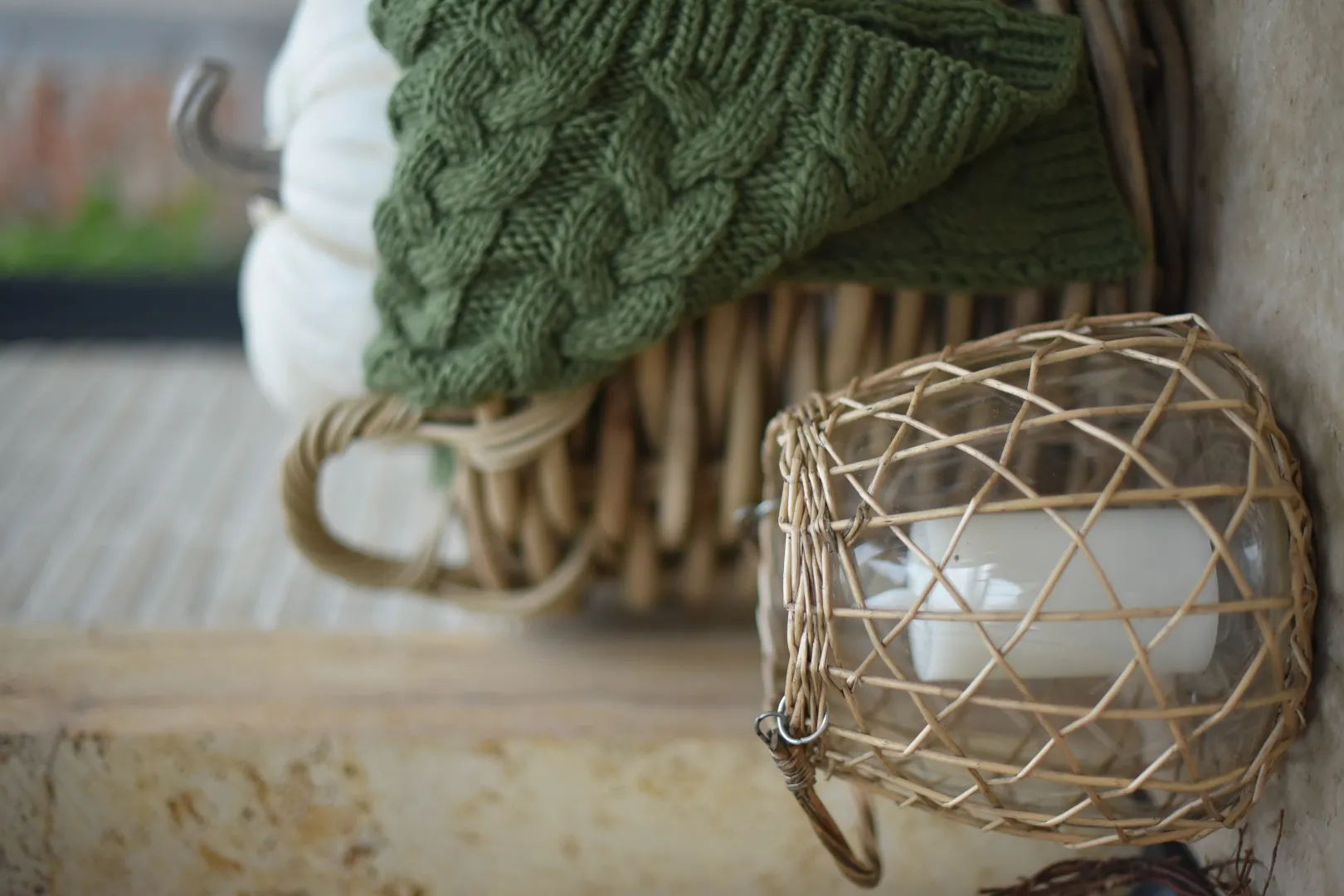 Décoration d'automne : photophore en rotin avec une bougie, un plaid vert en tricot et une citrouille décorative blanche