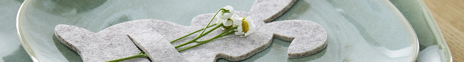 Osterdeko: grauer Filz-Hase mit kleinen weißen Blüten auf grünem Keramikteller