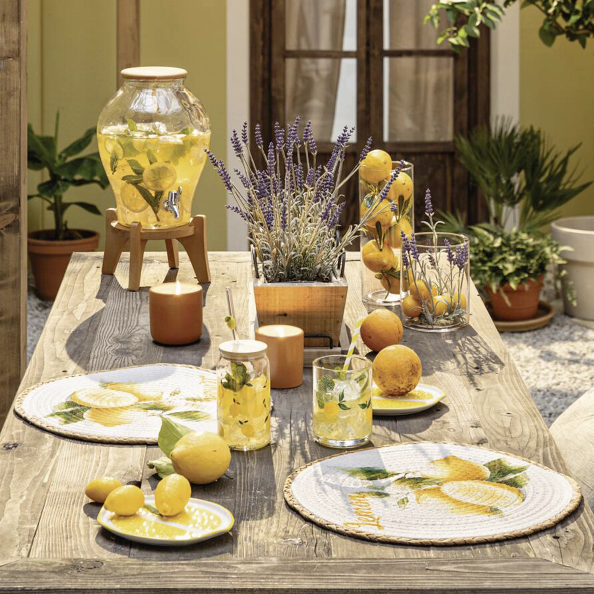 Sommerdeko: gedeckter Gartentisch mit Zitronen, Kerzen, Gläsern und floralen Tischaccessoires