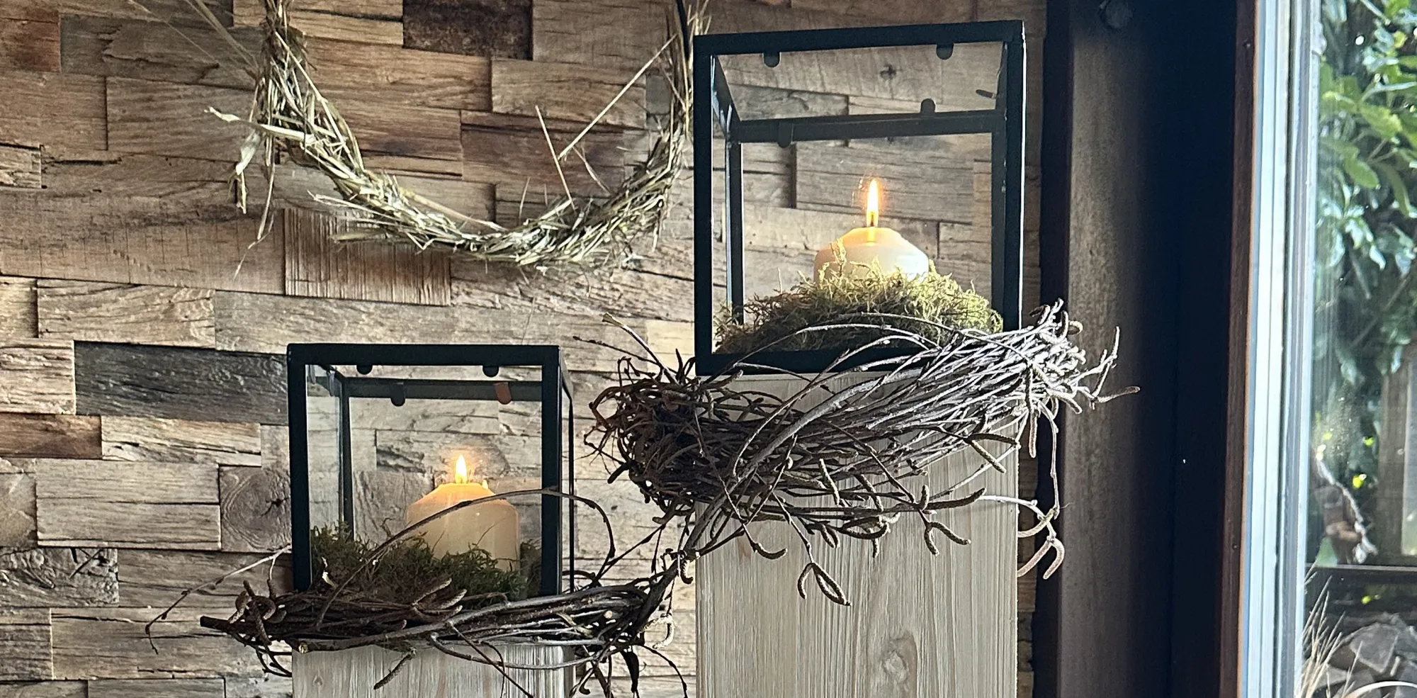 Décoration printanière : lanternes noires avec des bougies blanches dans des nids de mousse posés sur des piliers en bois clair