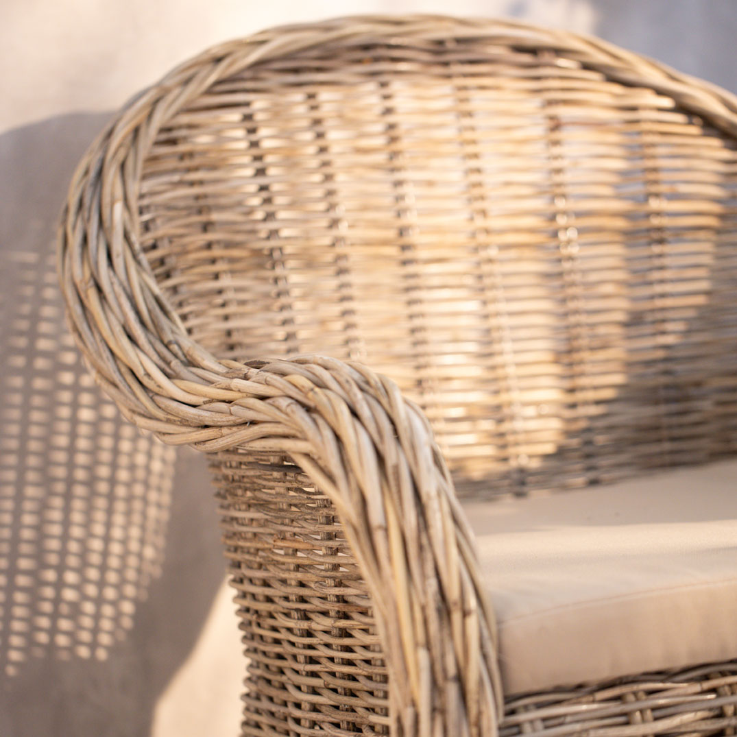 Gartenmöbel: naturfarbener Rattansessel mit hellem Sitzkissen als Outdoor-Sitzplatz