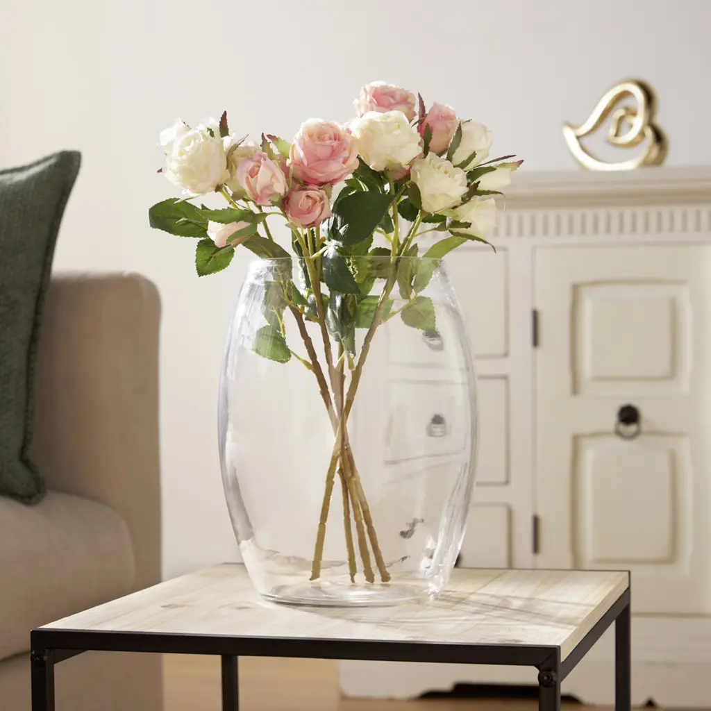 Des roses roses et crème dans un grand vase en verre posé sur une table d'appoint