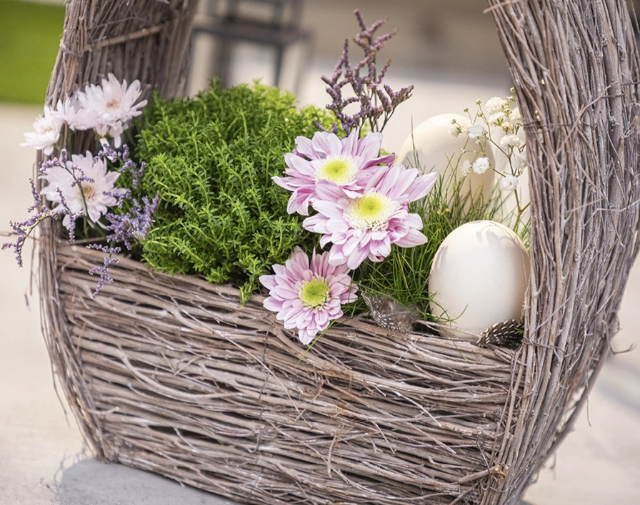 Pflanzkorb: grauer Pflanzkorb mit rosa Blumen, grünen Pflanzen und weißen Dekoeiern als Frühlingsdeko