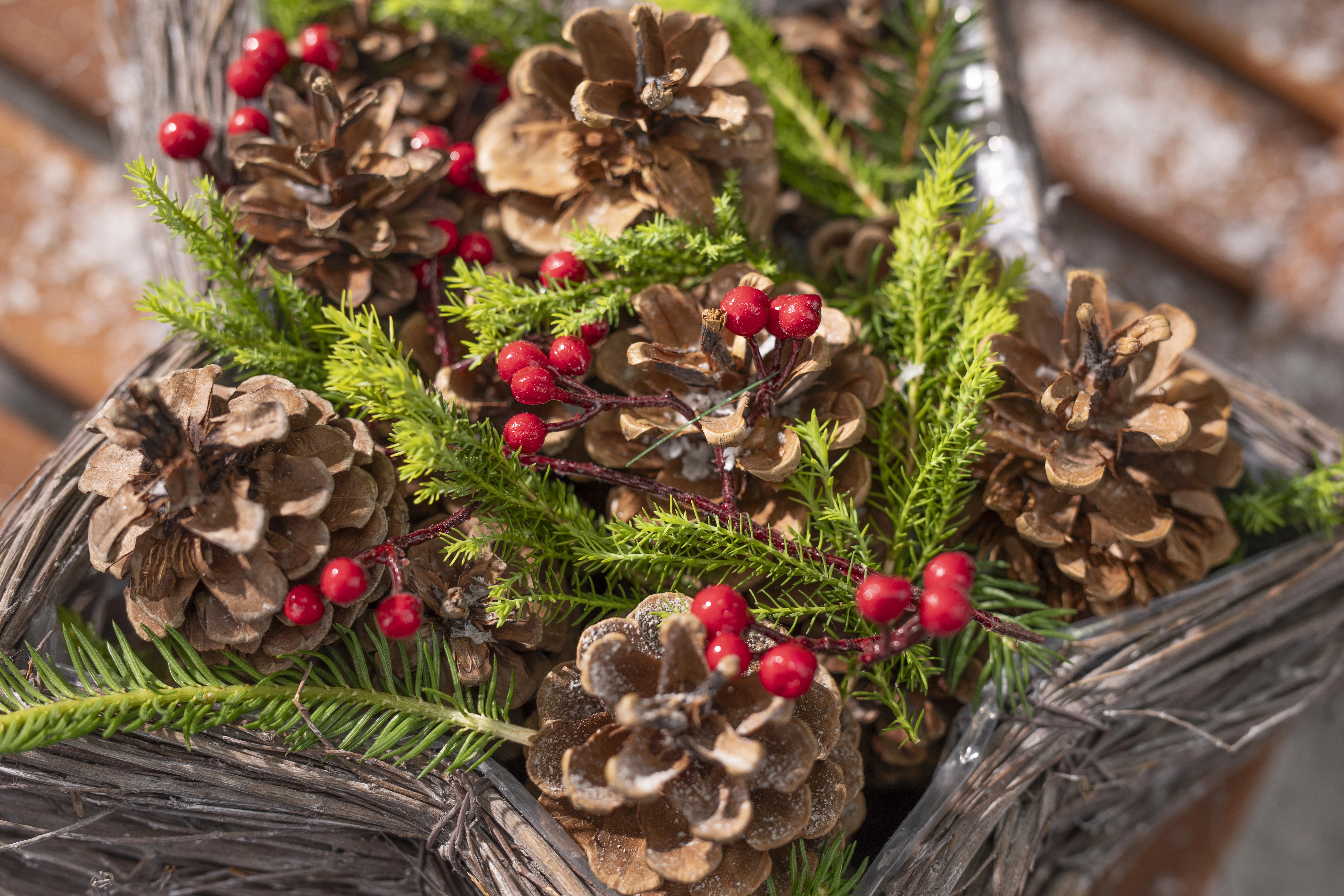 Composition de Noël composée de pommes de pin, de brindilles de sapin et de baies rouges, présentée dans un panier tressé en matériaux naturels