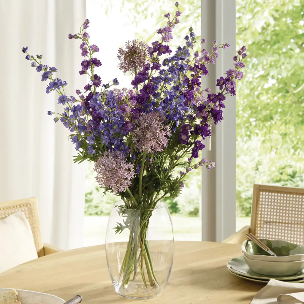 Bouquet de fleurs violettes et roses dans un vase en verre posé sur une table en bois