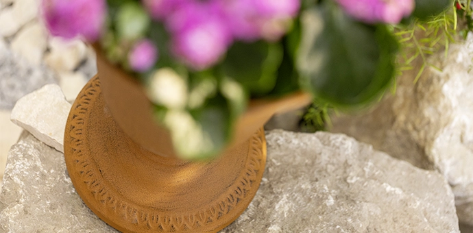 Rostdeko: rostfarbener Metall‑Blumentopf mit rosa Frühlingsblumen auf Natursteinen