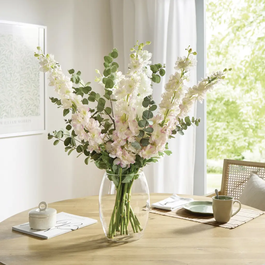 Bouquet lumineux composé de fleurs blanc-rose et d'eucalyptus dans un vase en verre