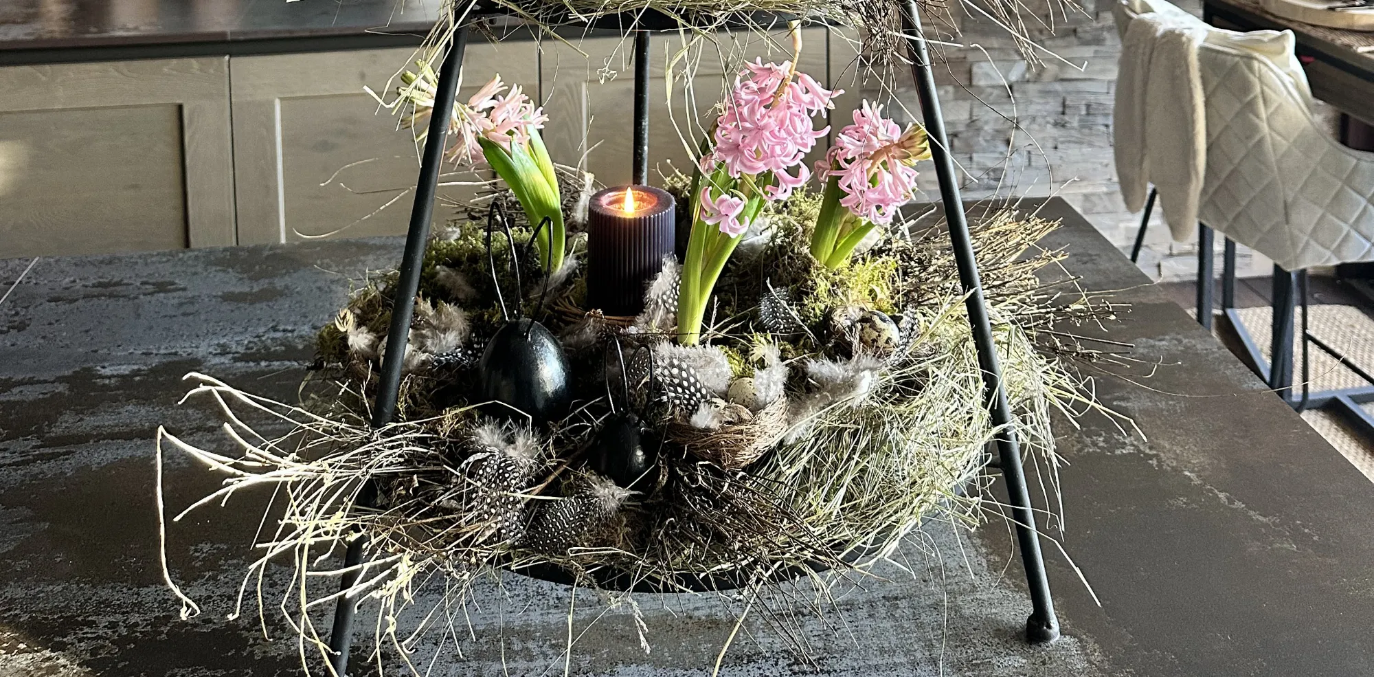 Décoration de Pâques : nid de mousse avec des jacinthes roses et des œufs décoratifs noirs dans un support métallique