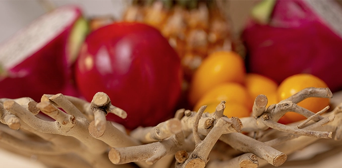 Décoration de table : corbeille en bois faite de brindilles avec un fruit du dragon rouge, une pomme et des fruits jaunes
