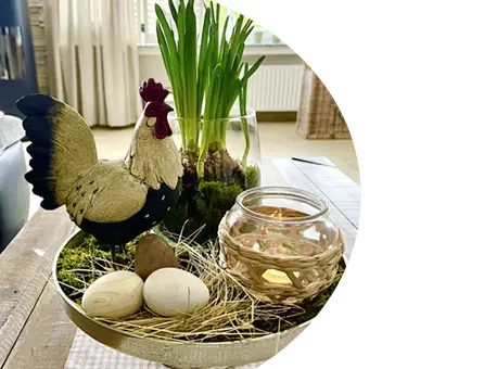 Décoration de Pâques sur un plateau avec une figurine de coq, une lanterne en verre, des œufs et des plantes printanières dans le salon
