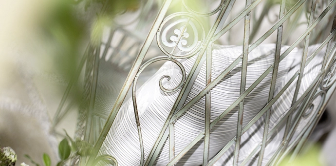 Detailaufnahme eines verzierten Metallgitters mit geschwungenen Ornamenten und dahinterliegendem Dekokissen in hellem Muster