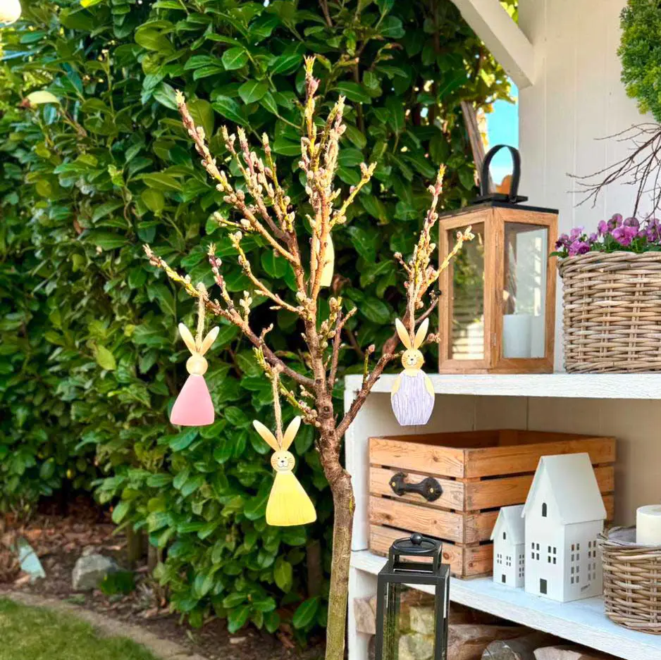 Décoration de Pâques : pendentifs lapins colorés sur une branche avec un panier à fleurs et des pâquerettes