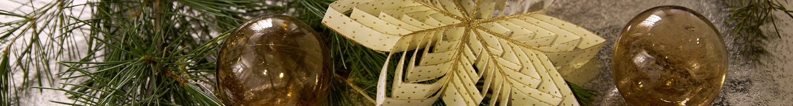 Décoration de Noël : fleur en papier dorée accompagnée de boules de Noël et de branches de sapin pour une décoration festive