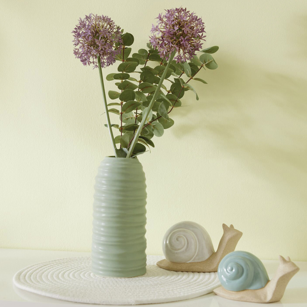 Zwei Alliumblüten in hoher grüner Vase mit Deko-Schnecken