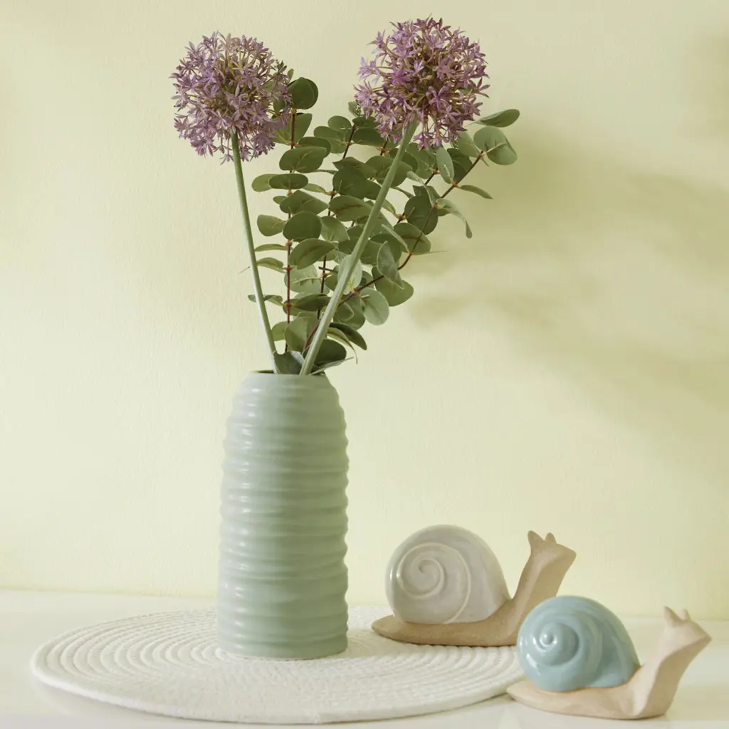 Deux fleurs d'allium dans un grand vase vert orné d'escargots décoratifs