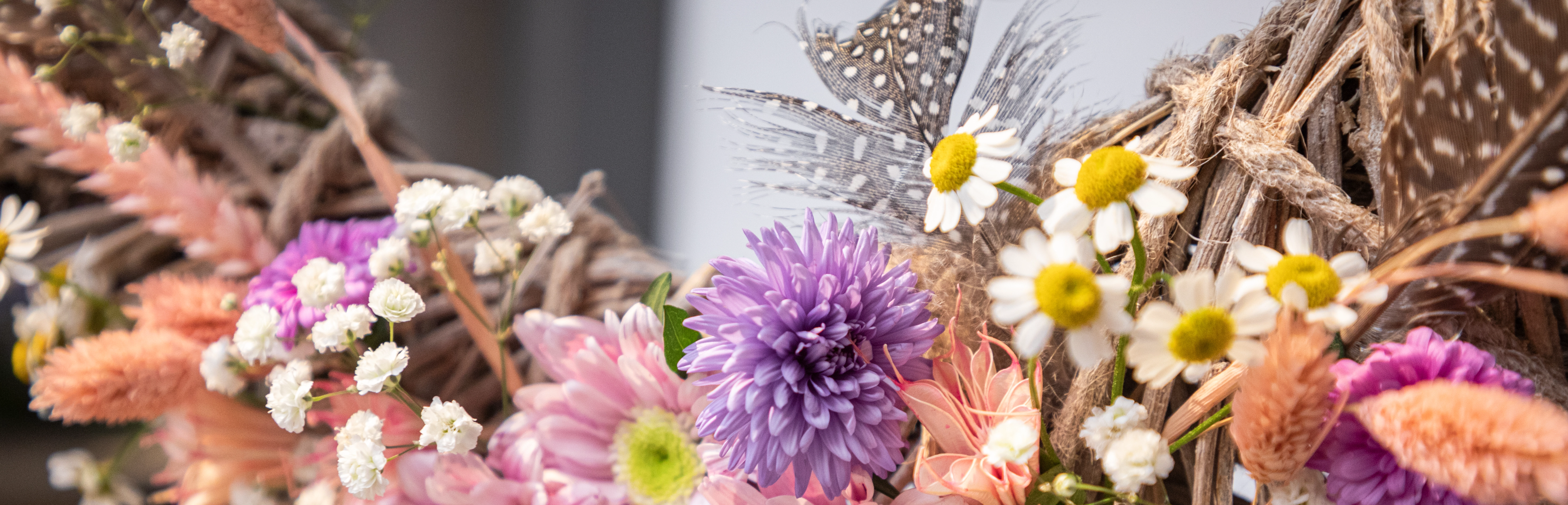 Dekokranz: geflochtener Kranz mit rosa, lila und weißen Blumen sowie Federn als Frühlingsdeko