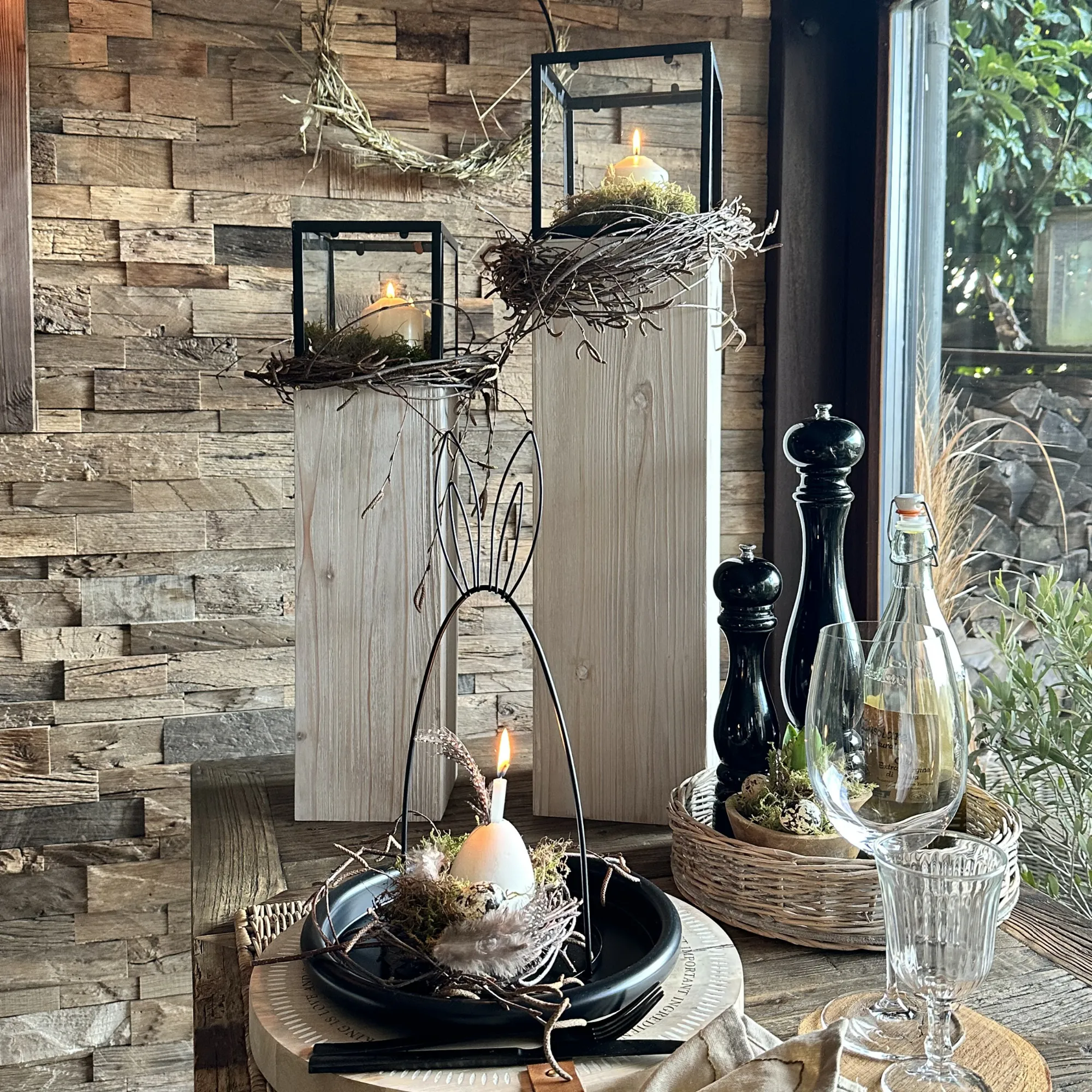 Décoration printanière : lanternes noires avec des nids de mousse et des bougies blanches sur des socles en bois