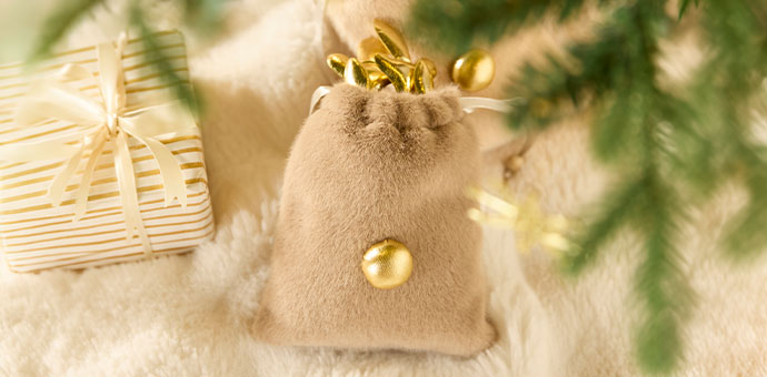 Décoration de Noël : petit sac en velours beige avec des boules de Noël dorées posées sur une fourrure douce