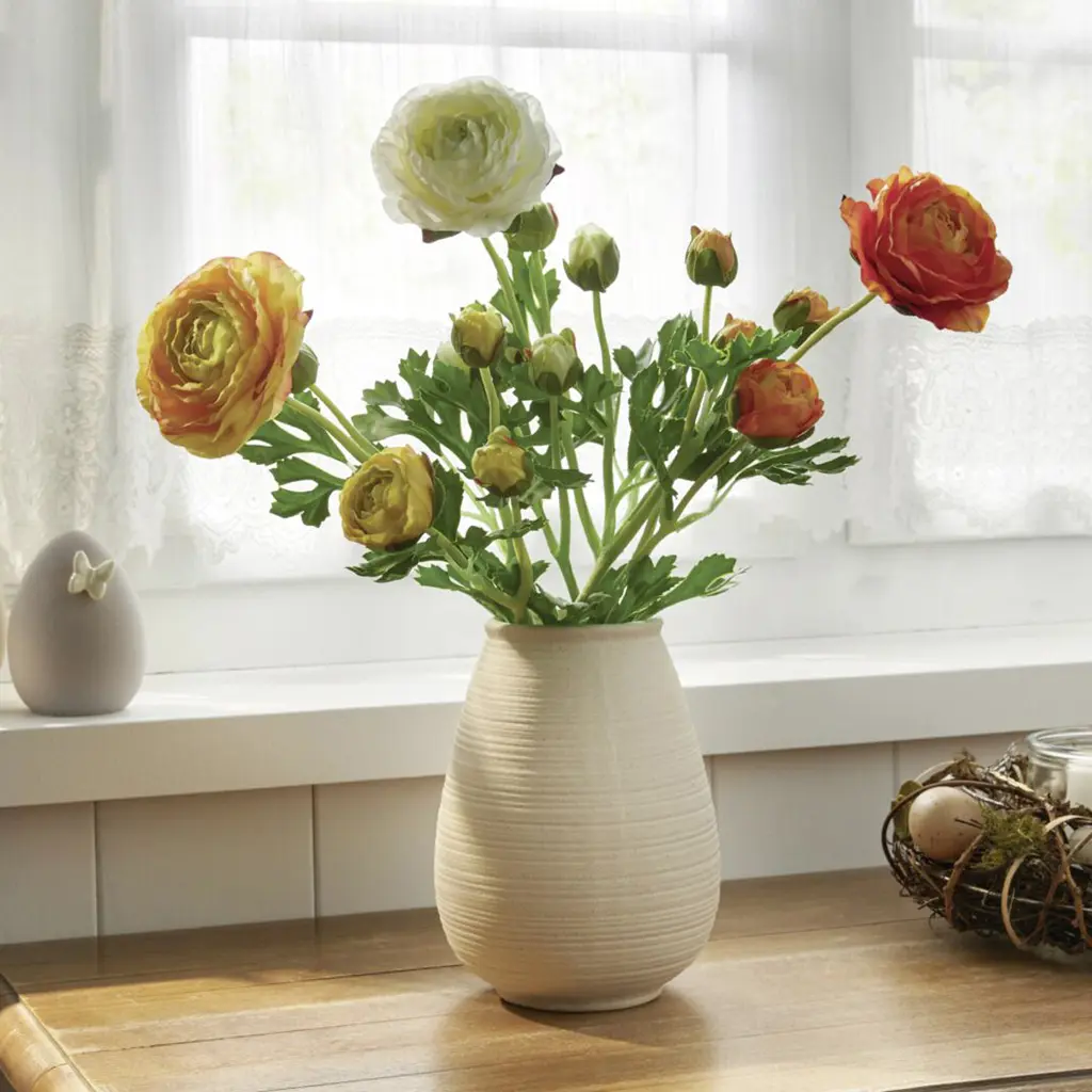 Bouquet de renoncules aux couleurs chaudes dans un vase crème près de la fenêtre