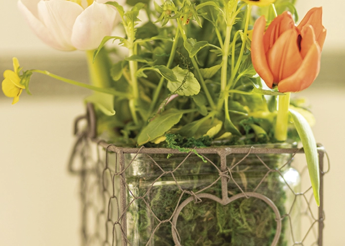 Frühlingsdeko: Glasvase im Drahtkorb mit weißen und orangefarbenen Tulpen als natürliche Wohnraumdeko