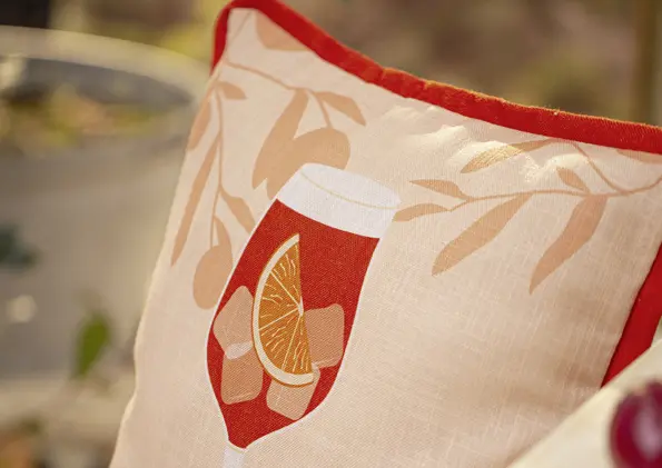 Chèque-cadeau orné d'une housse de coussin représentant une boisson estivale, une rondelle d'orange et des glaçons, dans des tons chauds de rouge et de beige