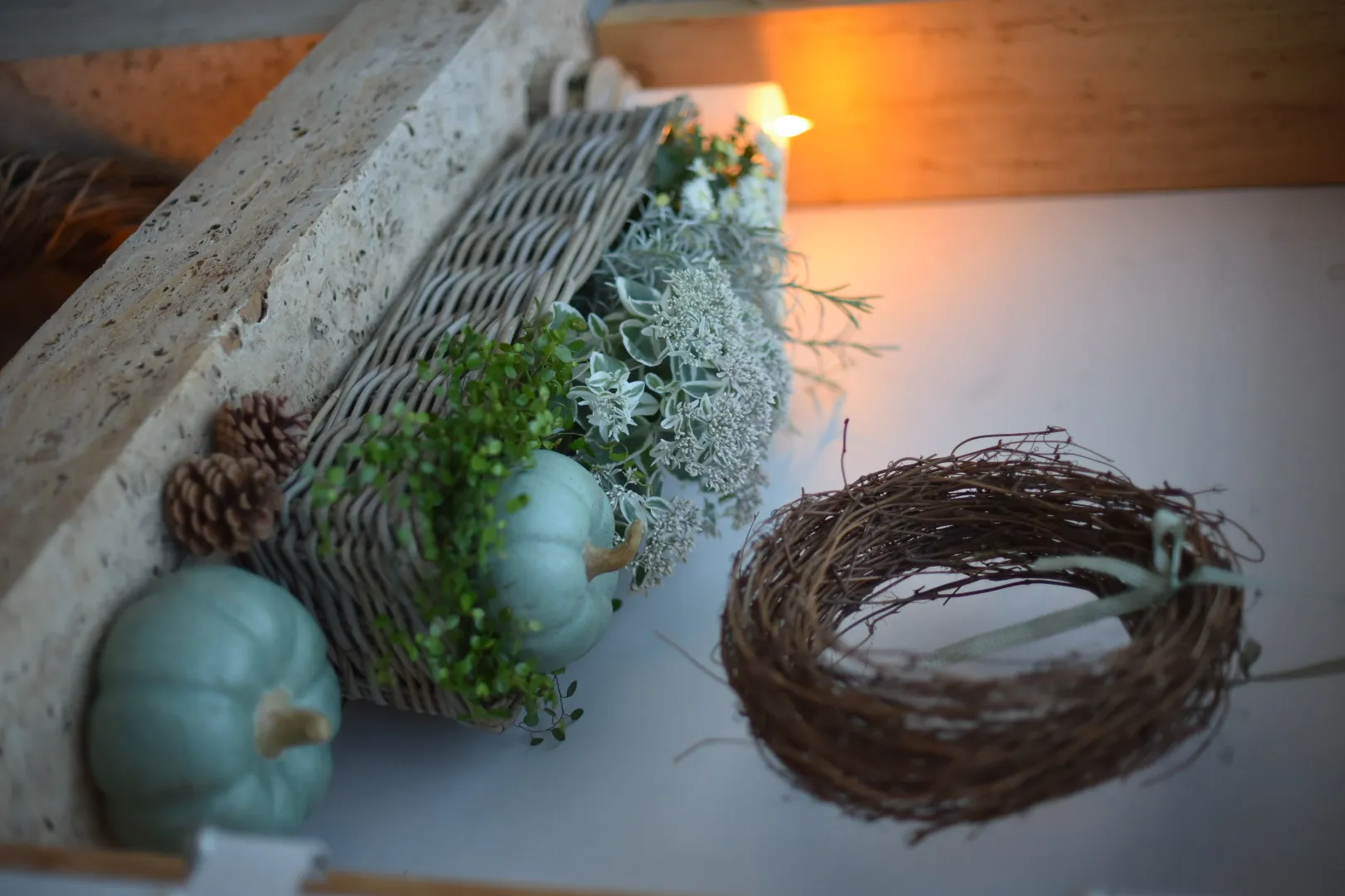 Décoration d'automne : citrouilles décoratives grises dans un panier en osier, accompagnées d'une couronne naturelle et de fleurs blanches