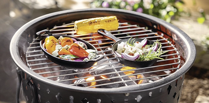 Grilldeko: runder Garten‑Grill mit Pfännchen, gegrilltem Gemüse und Mais für Sommerabende