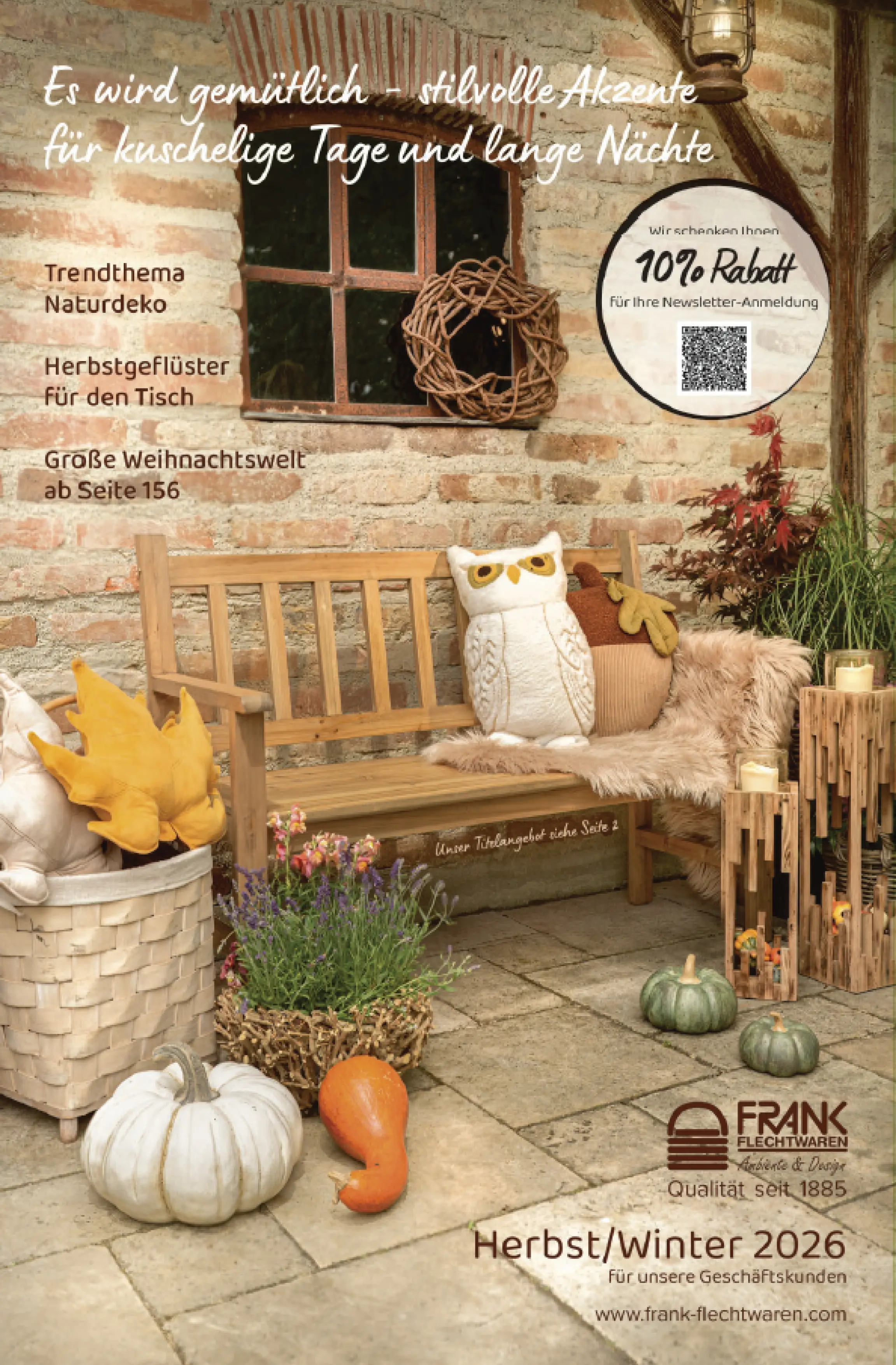 Décor d’extérieur automnal : banc en bois, citrouilles, coussins chouettes, lanternes, panier tressé et plantes devant un mur de briques rustique — couverture catalogue Automne/Hiver 2026 pro