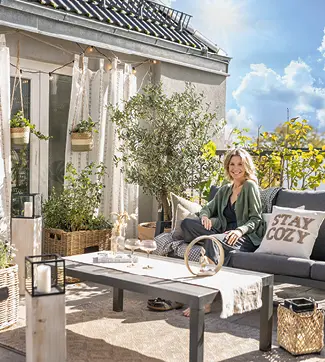 Frau, die lächelnd auf einem frühlingshaft dekorierten Balkon sitzt