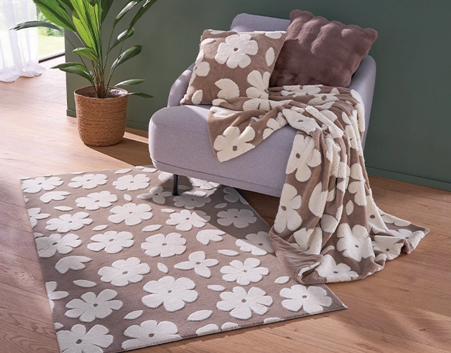 Wohntextilien: Teppich, Kissen und Decke in Beige mit weißen Blumen als gemütliche Wohnzimmerdeko