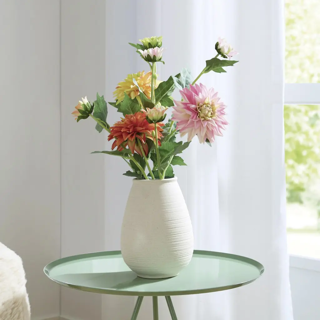 Bouquet de dahlias colorés dans un vase crème posé sur une table ronde